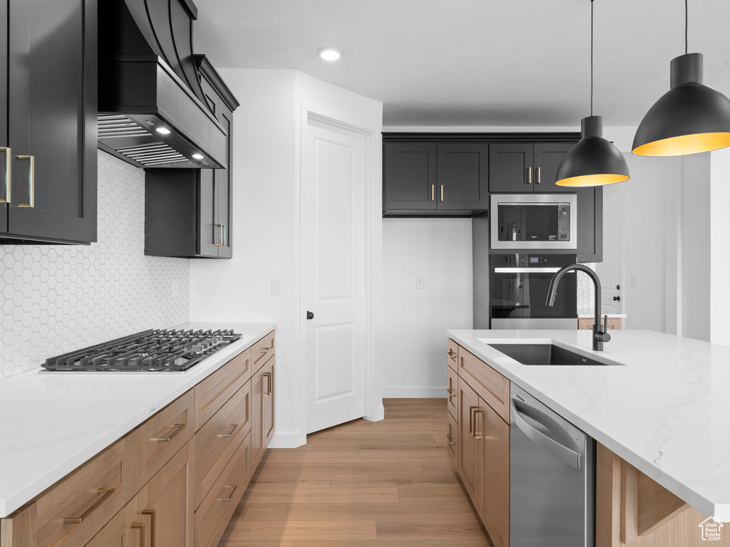 Kitchen featuring pendant lighting, custom range hood, a sink, appliances with stainless steel finishes, and light wood finished floors