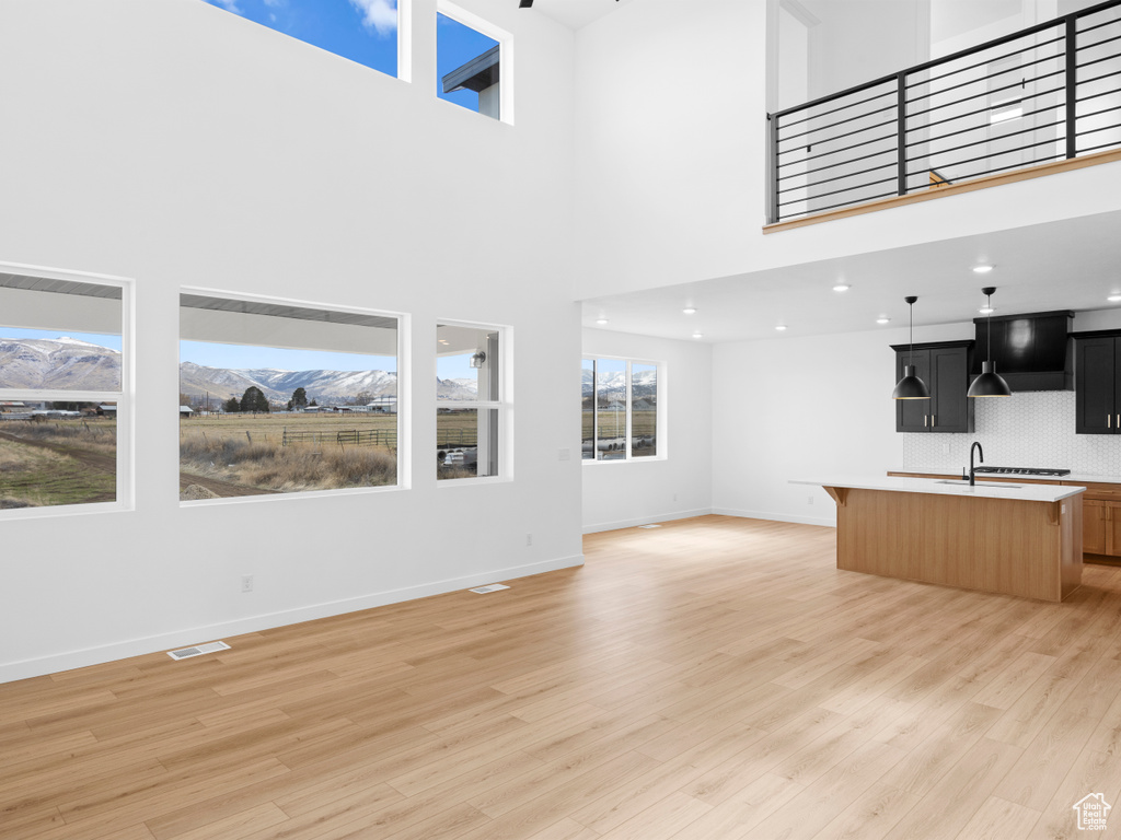 Unfurnished living room featuring visible vents, baseboards, light wood-type flooring, a mountain view, and a sink