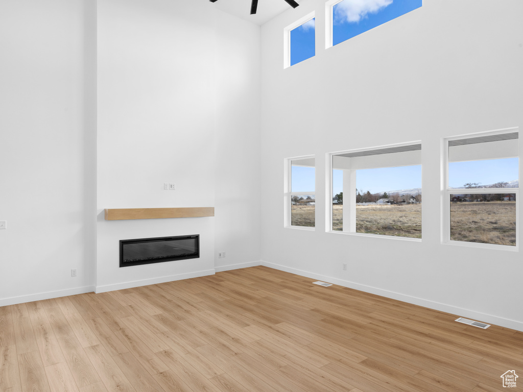 Unfurnished living room featuring a glass covered fireplace, light wood-style flooring, plenty of natural light, and visible vents