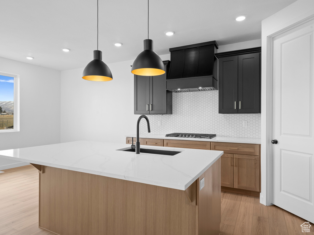 Kitchen with light wood finished floors, premium range hood, light stone counters, gas stovetop, and a sink