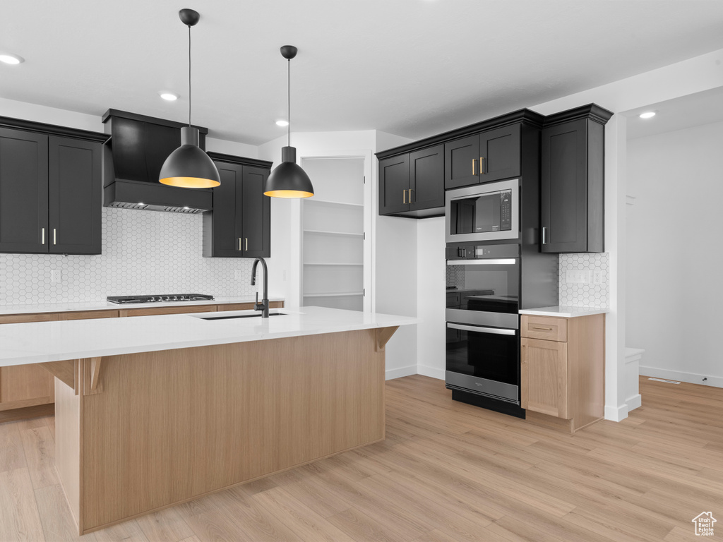 Kitchen with stainless steel microwave, light countertops, light wood-style flooring, gas cooktop, and a sink