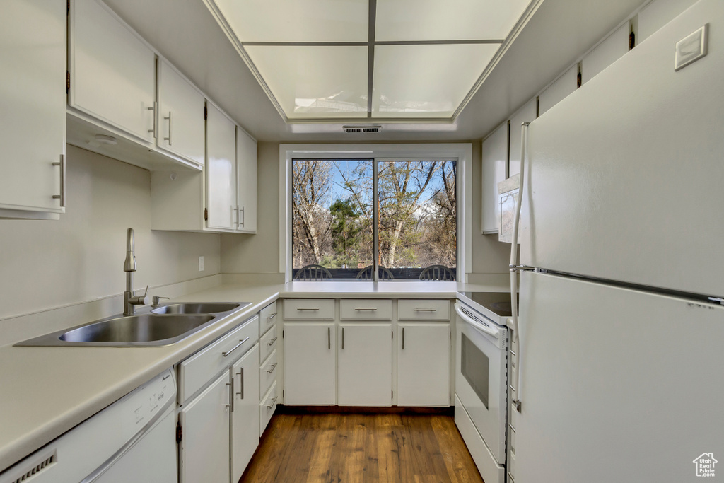Kitchen featuring a sink, dark wood-style floors, white appliances, white cabinets, and light countertops