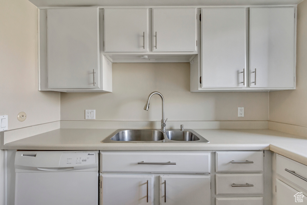 Kitchen featuring light countertops, white cabinets, white dishwasher, and a sink