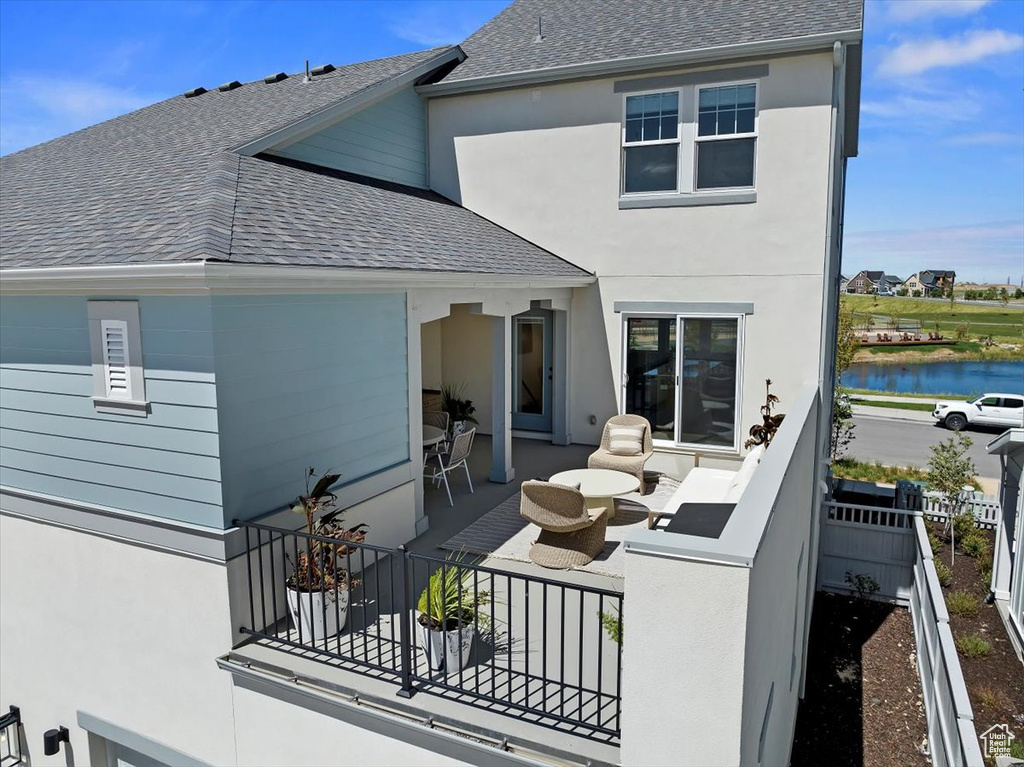 Back of property with a patio, fence, roof with shingles, stucco siding, and a water view