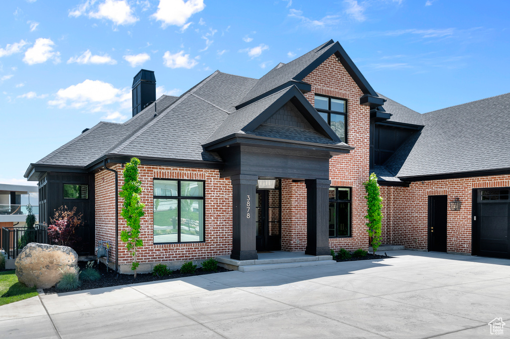 View of front of home with brick siding, roof with shingles, and a chimney