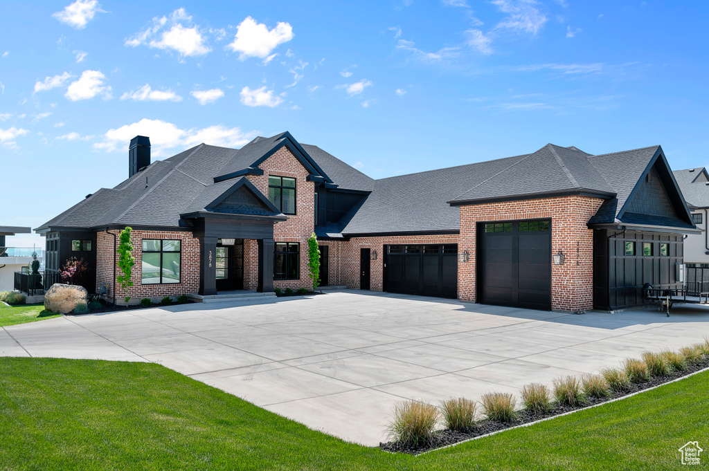 View of front facade featuring brick siding, driveway, a garage, a shingled roof, and a chimney