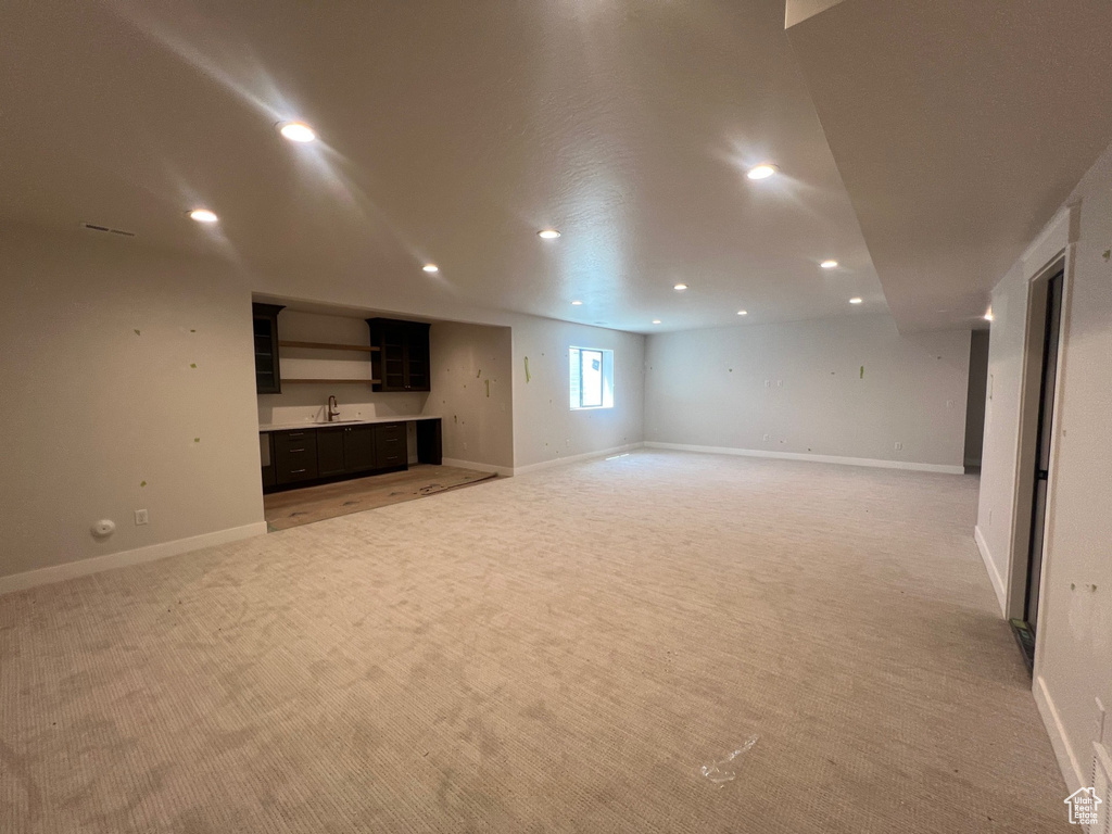 Unfurnished living room with light colored carpet, recessed lighting, and wet bar