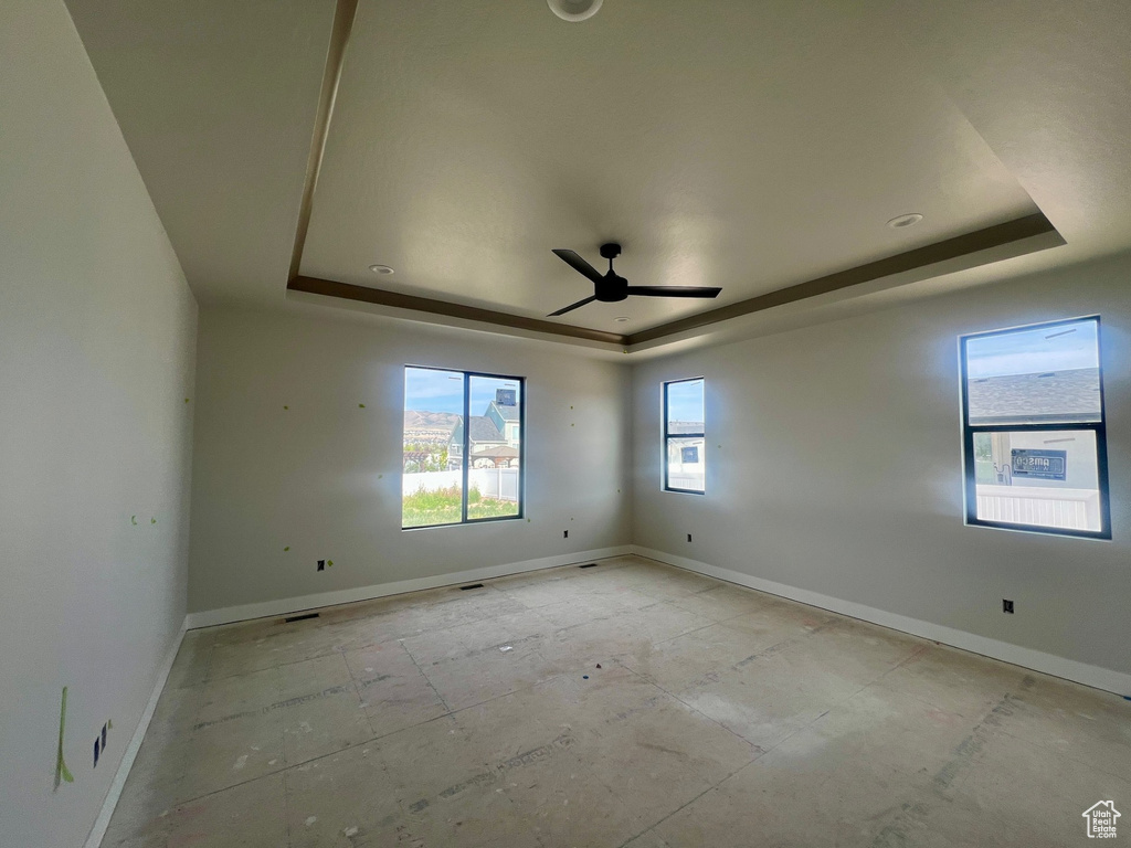 Empty room with a raised ceiling, ceiling fan, and baseboards