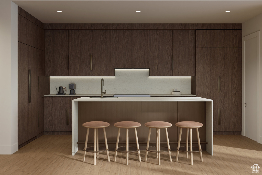 Kitchen featuring light wood-type flooring, modern cabinets, a center island with sink, a sink, and light countertops