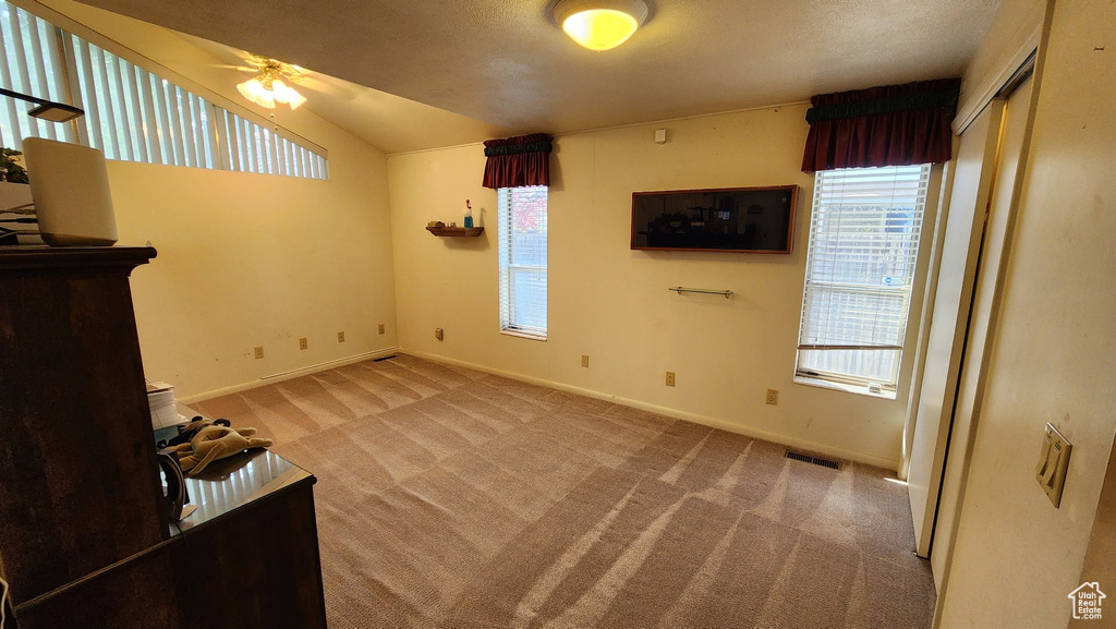 Unfurnished living room with carpet flooring, visible vents, baseboards, ceiling fan, and vaulted ceiling