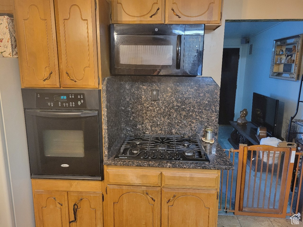 Kitchen with dark stone counters, backsplash, black appliances, and brown cabinetry