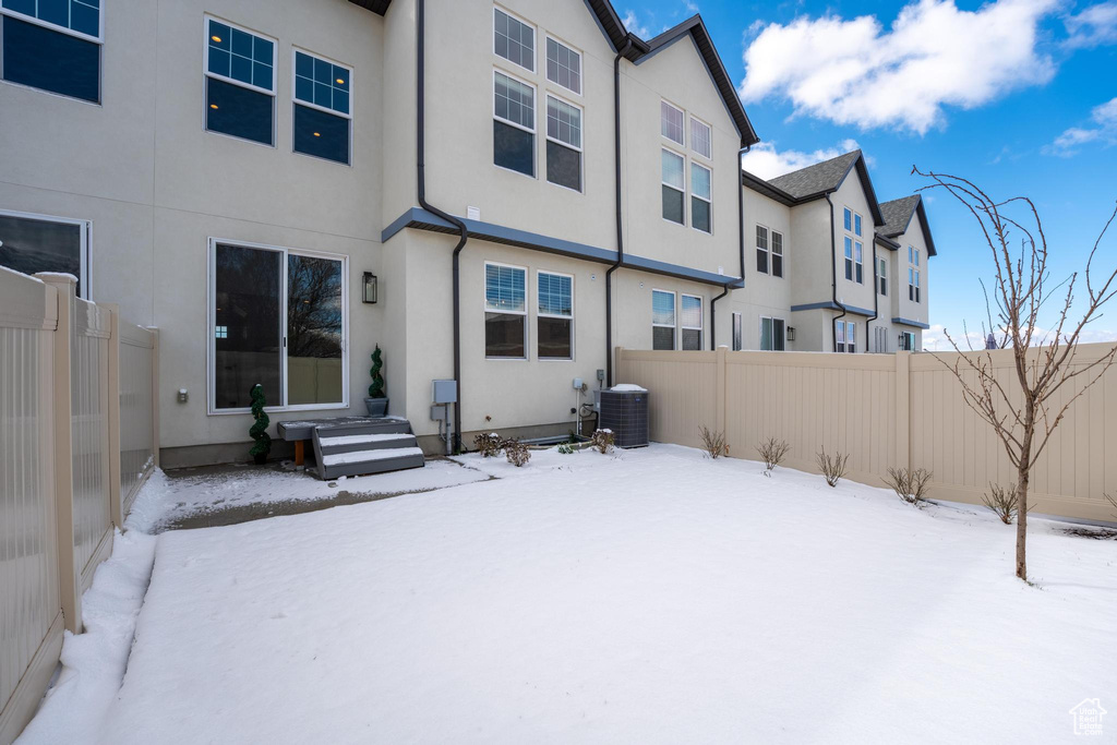 Snow covered rear of property with stucco siding, central AC unit, and fence