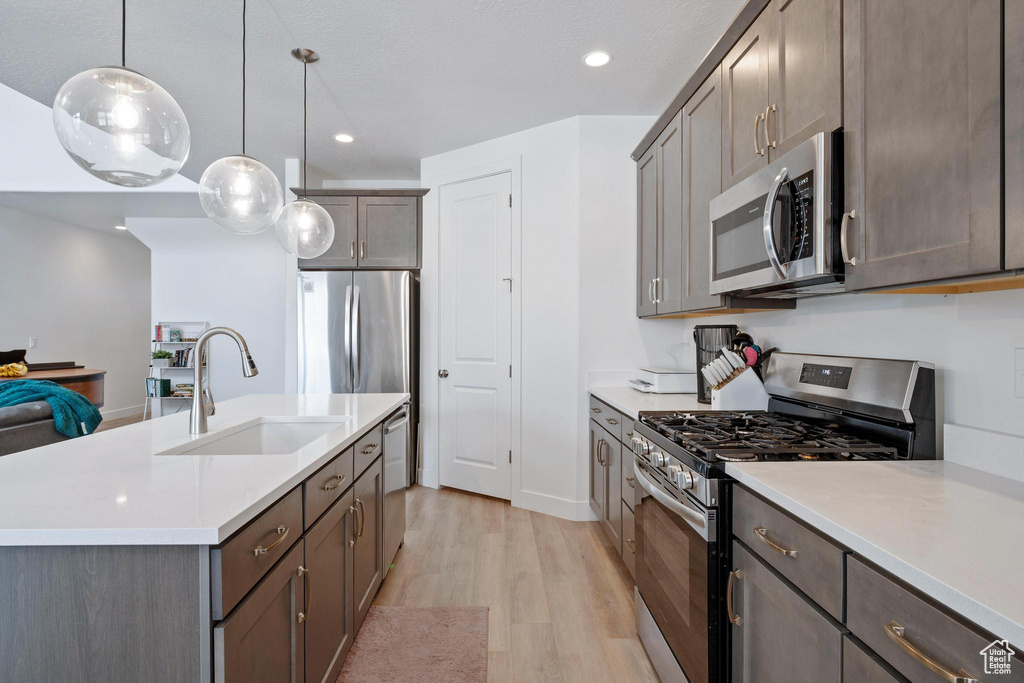 Kitchen with an island with sink, light countertops, light wood-style flooring, appliances with stainless steel finishes, and a sink