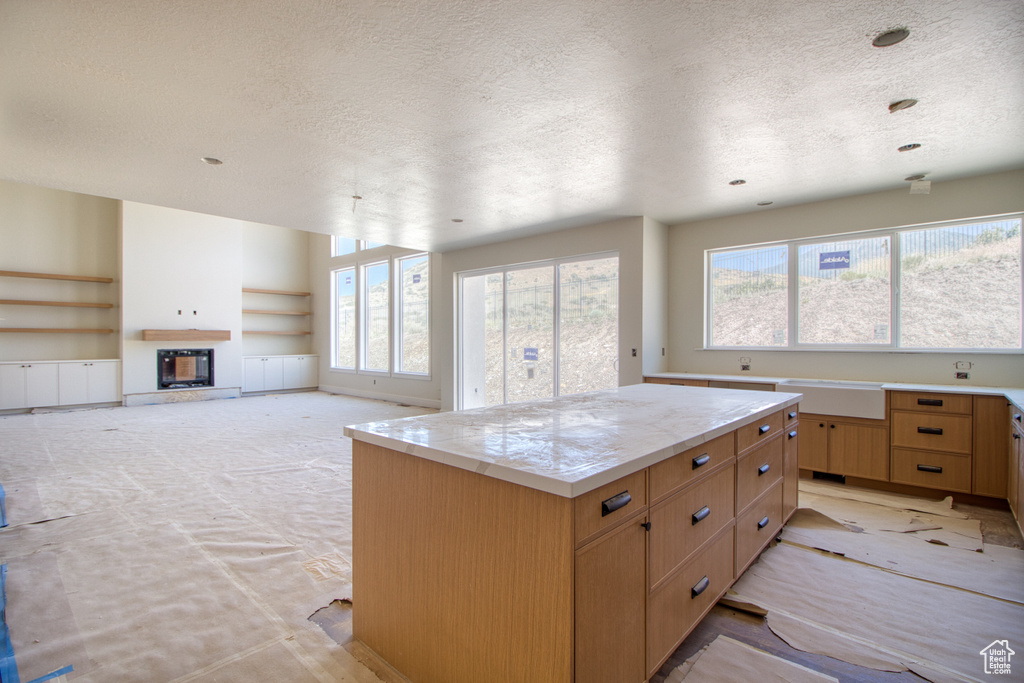 Kitchen with a textured ceiling, built in shelves, a glass covered fireplace, light countertops, and a kitchen island
