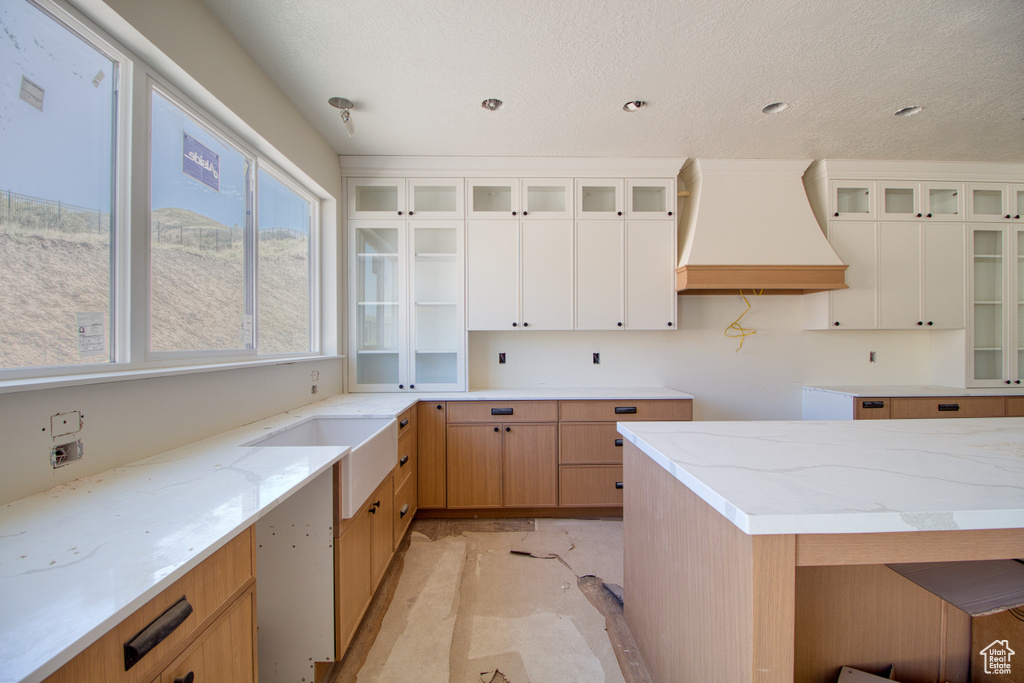 Kitchen featuring premium range hood, light stone counters, glass insert cabinets, white cabinets, and a textured ceiling