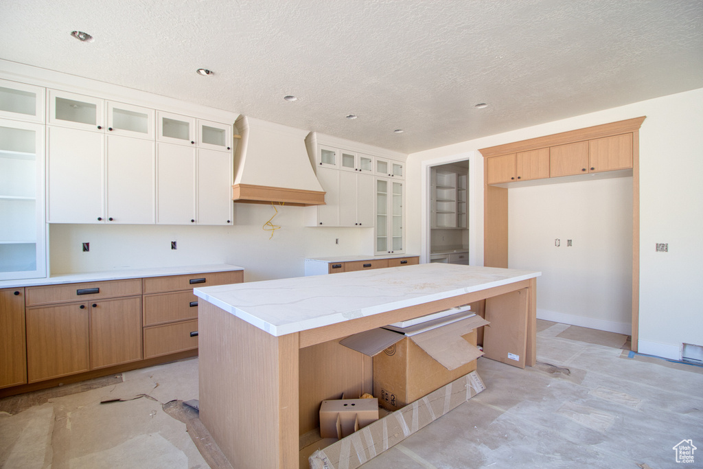 Kitchen with custom exhaust hood, glass insert cabinets, a textured ceiling, and white cabinets
