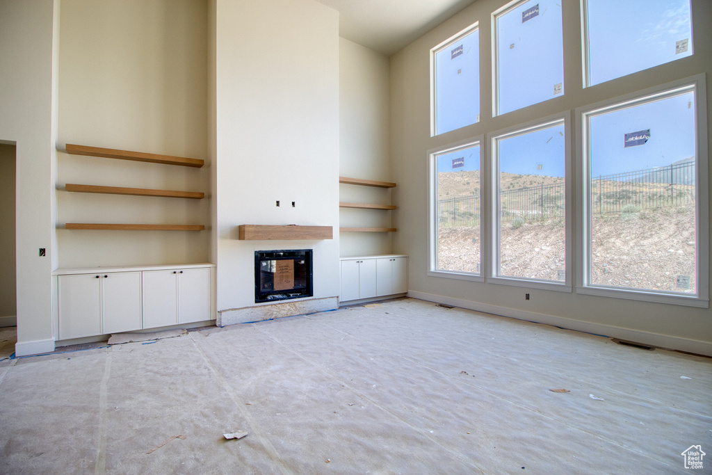 Unfurnished living room featuring built in shelves, a towering ceiling, a glass covered fireplace, and heating unit