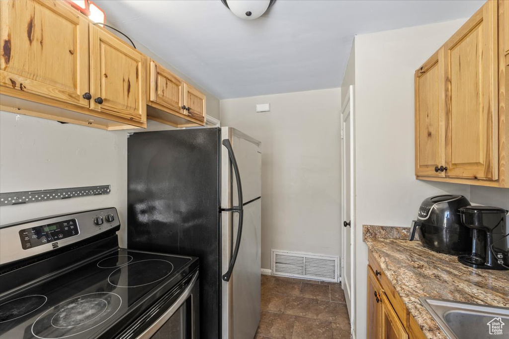 Kitchen featuring light brown cabinets, visible vents, stone countertops, a sink, and stainless steel appliances