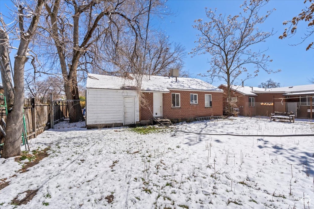 Snow covered property featuring brick siding, a chimney, and fence