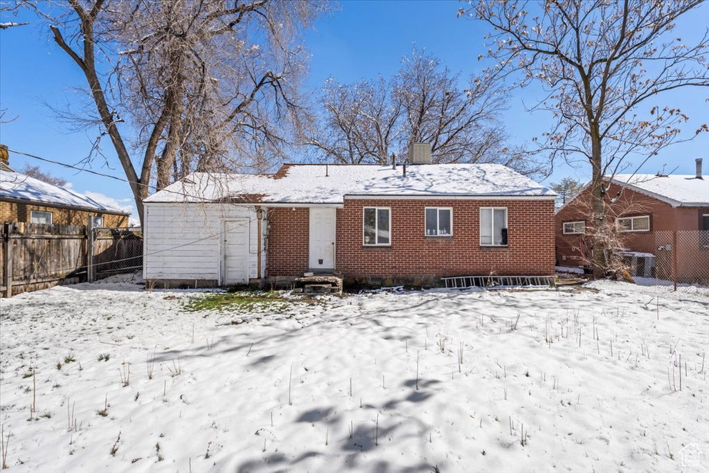Snow covered rear of property with fence and brick siding
