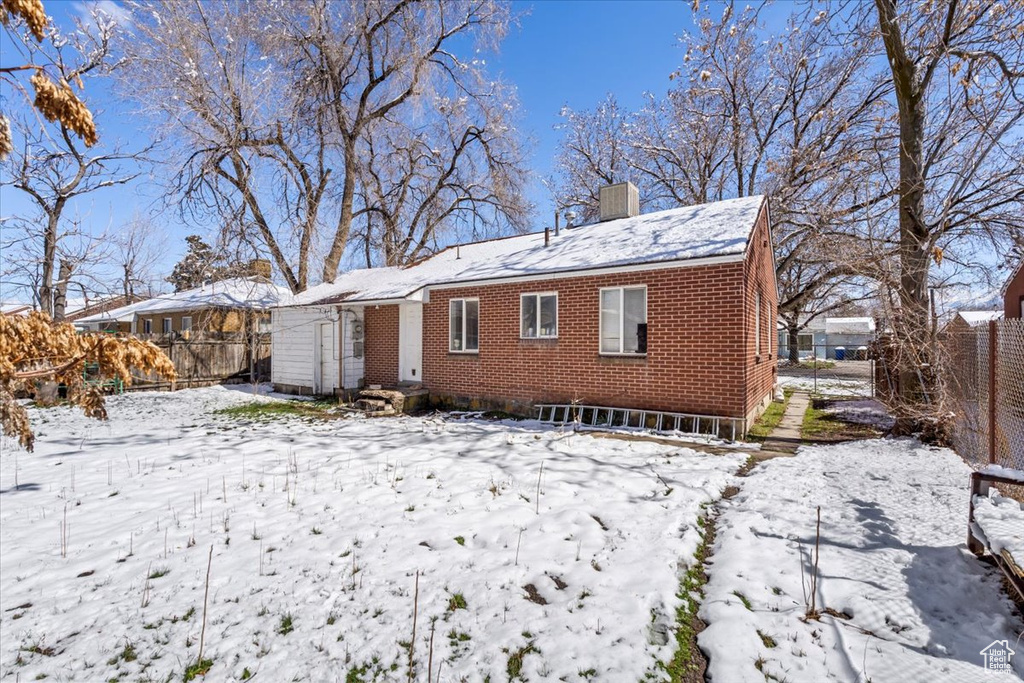 Snow covered rear of property featuring brick siding, a chimney, and fence