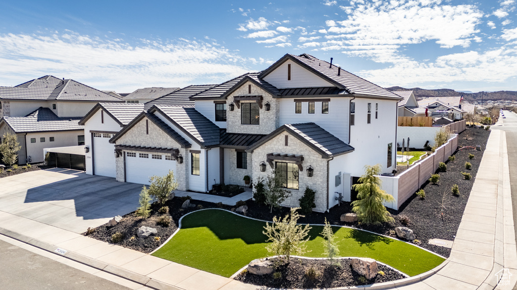 View of front facade with a standing seam roof, stone siding, fence, concrete driveway, and a garage