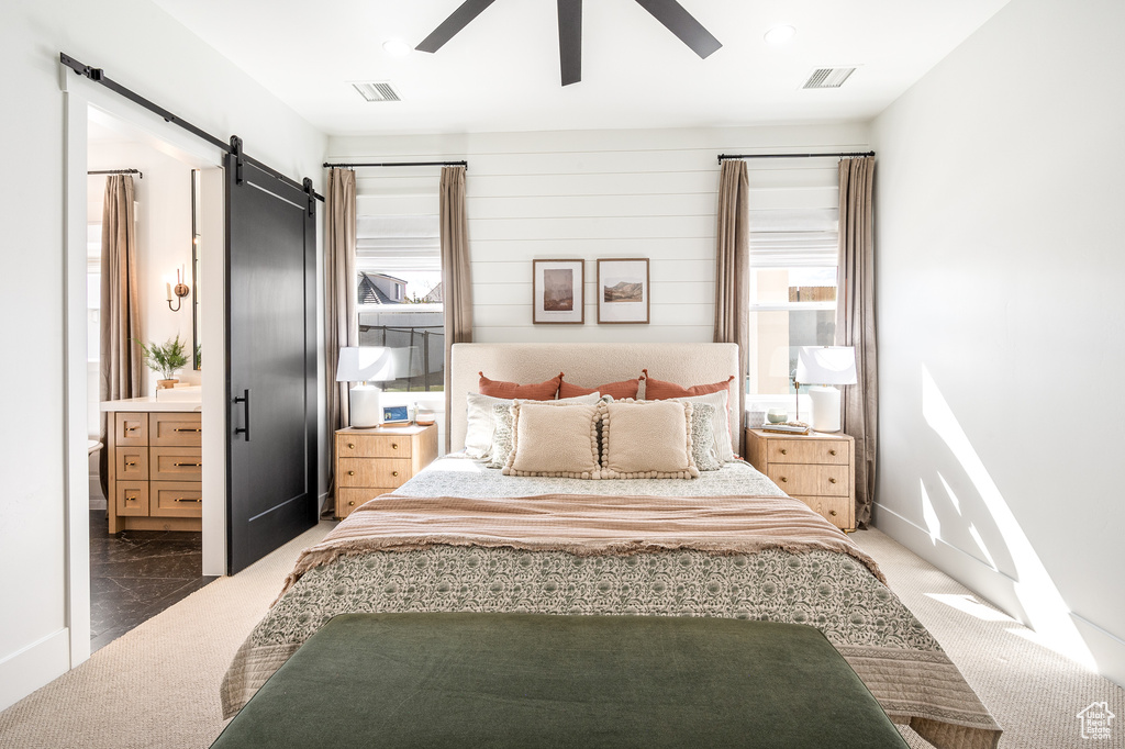 Carpeted bedroom featuring a barn door, visible vents, ensuite bathroom, and ceiling fan
