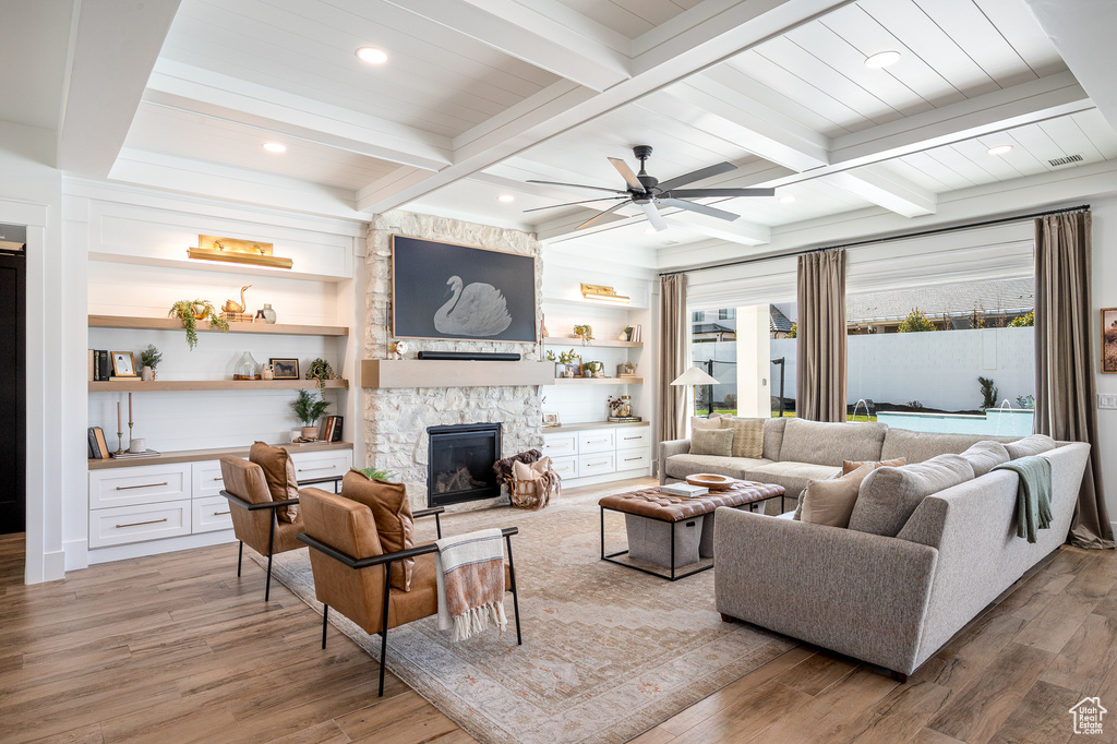 Living area featuring light wood-type flooring, beam ceiling, ceiling fan, and a fireplace