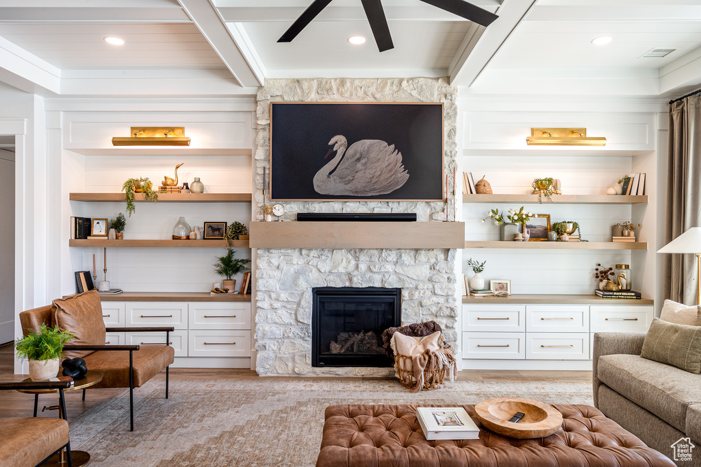 Living room featuring built in features, a ceiling fan, visible vents, beam ceiling, and a stone fireplace