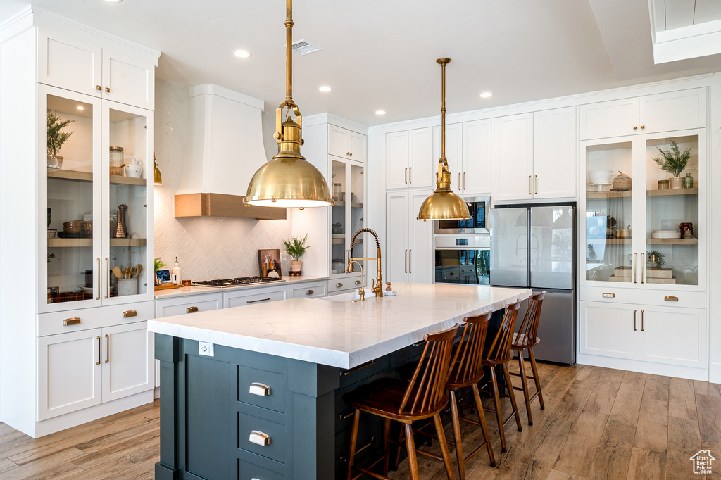 Kitchen featuring premium range hood, a sink, stainless steel appliances, white cabinetry, and light wood-type flooring