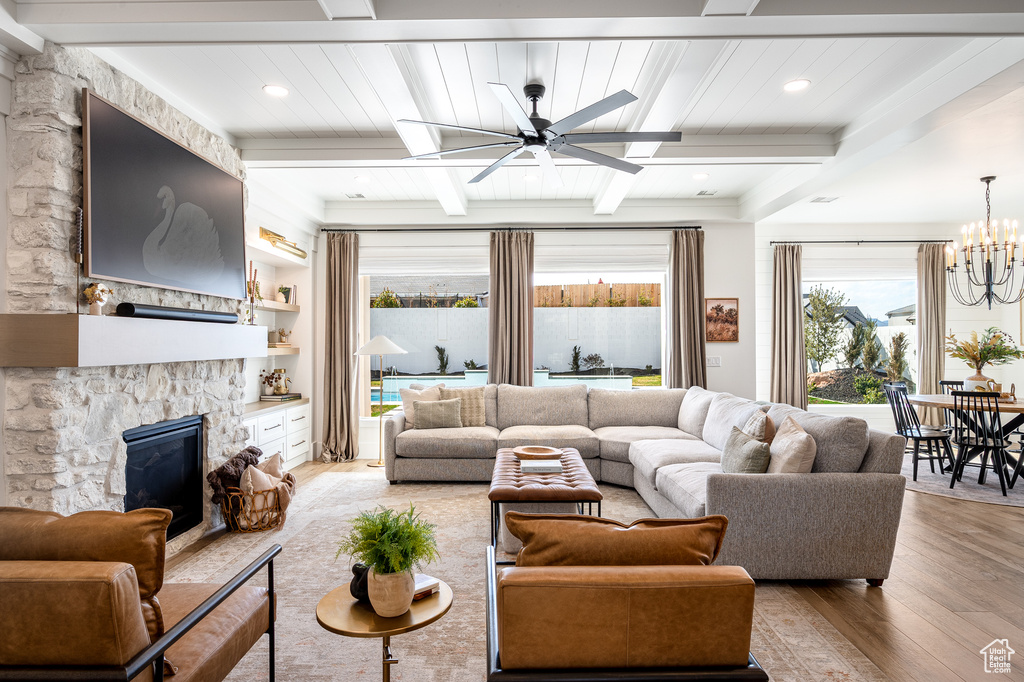 Living area with beamed ceiling, wood finished floors, a fireplace, and ceiling fan with notable chandelier
