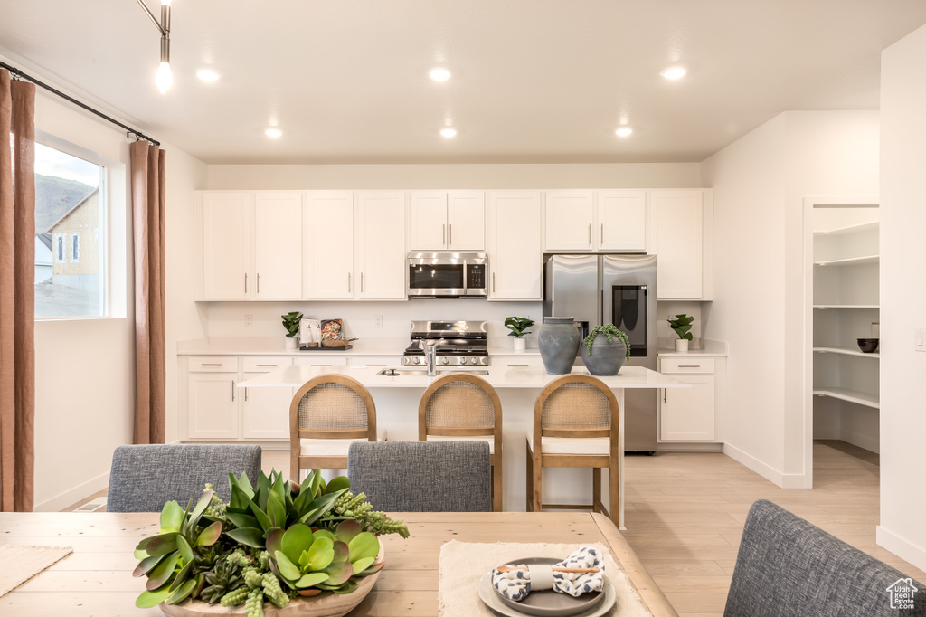 Kitchen featuring appliances with stainless steel finishes, white cabinetry, light countertops, and light wood-style floors