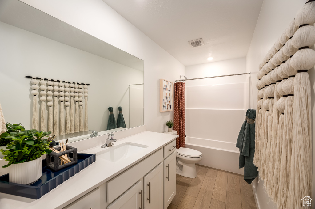 Bathroom with vanity, wood finished floors, visible vents, shower / bath combo with shower curtain, and toilet