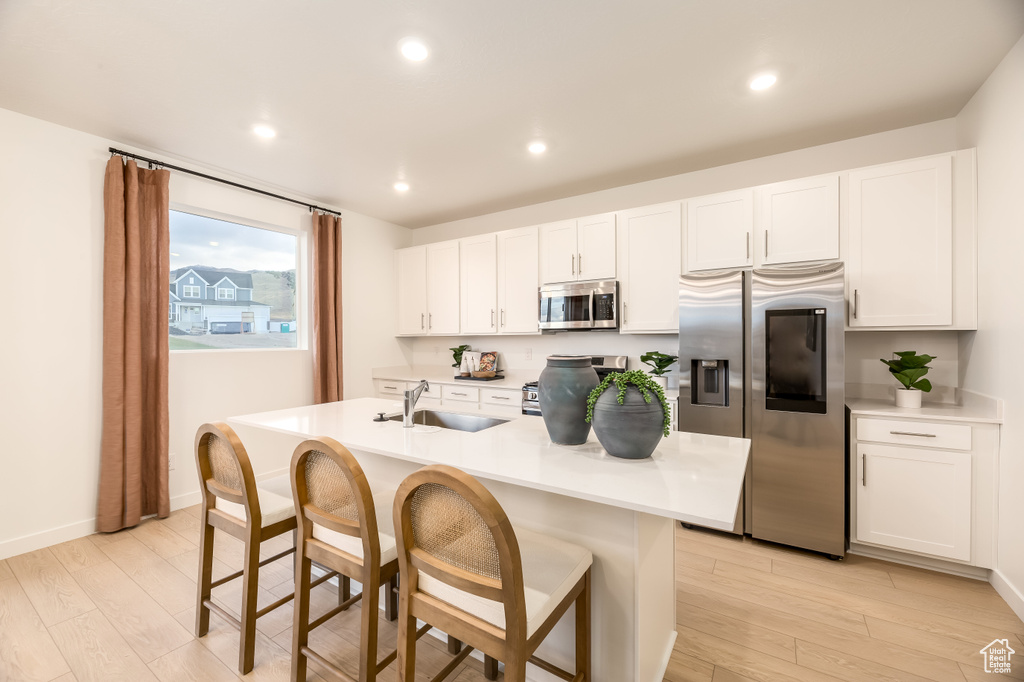 Kitchen featuring a breakfast bar area, light wood finished floors, a sink, stainless steel appliances, and white cabinets