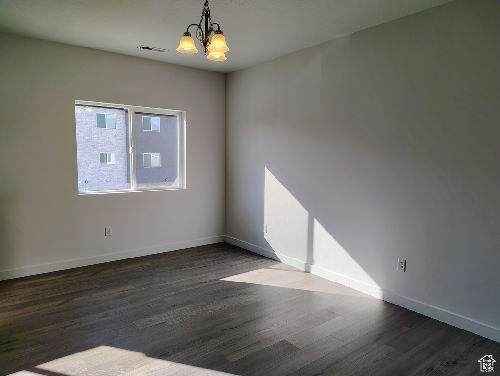Empty room with dark wood-type flooring, visible vents, baseboards, and a chandelier