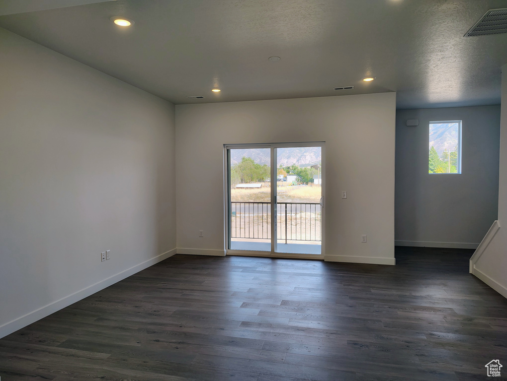 Empty room with dark wood-style floors, visible vents, recessed lighting, and baseboards