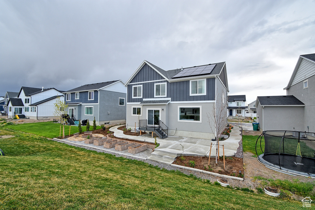 Back of property featuring a patio, a trampoline, a residential view, and roof mounted solar panels