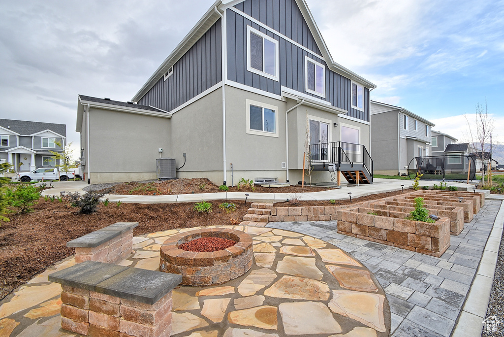Rear view of house with board and batten siding, a fire pit, a residential view, a patio area, and cooling unit