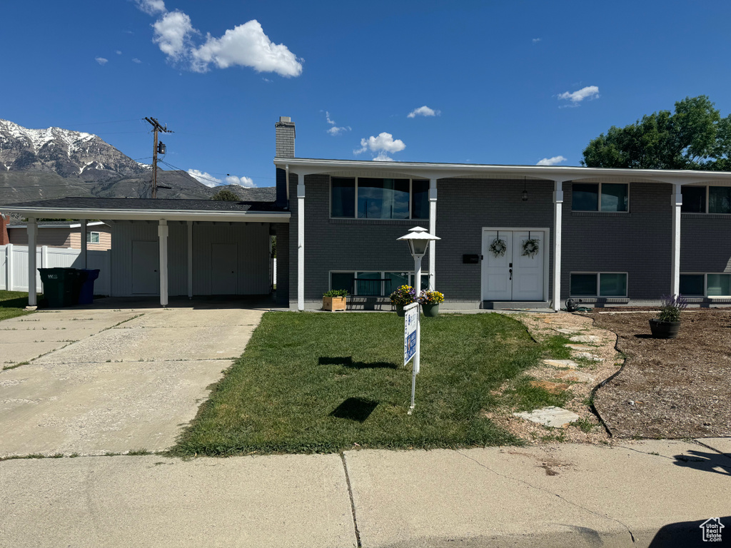 View of front facade with a chimney, a carport, concrete driveway, brick siding, and a front yard