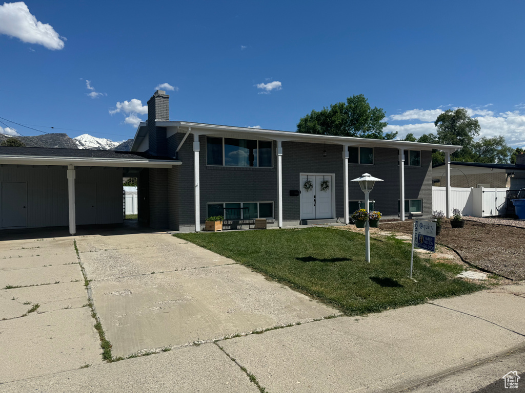 Bi-level home featuring a chimney, concrete driveway, a carport, and brick siding