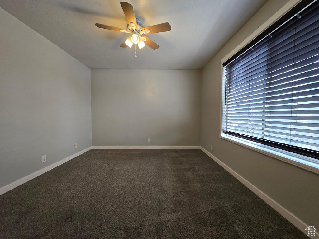 Empty room with baseboards, ceiling fan, and dark colored carpet