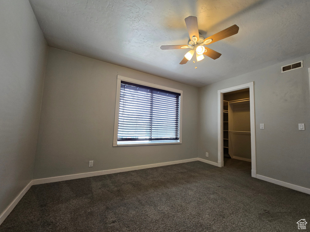 Unfurnished bedroom with visible vents, a walk in closet, baseboards, ceiling fan, and dark carpet