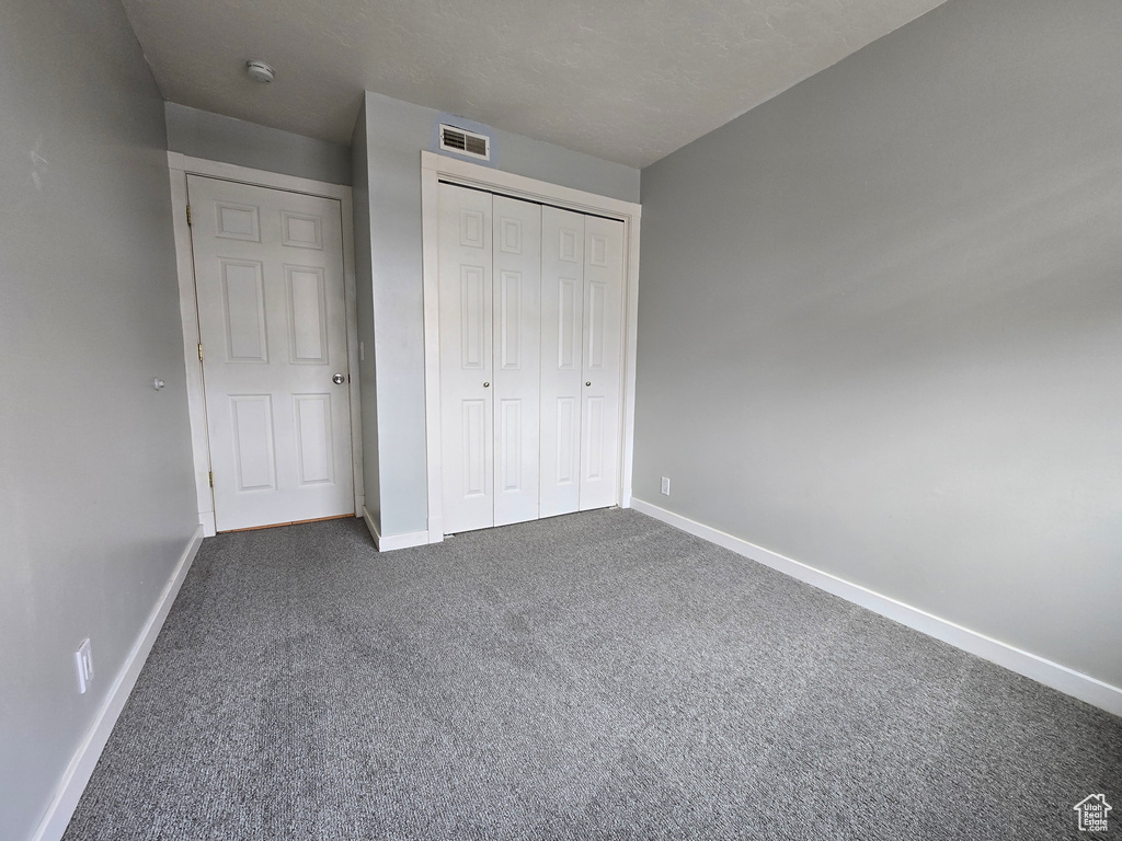 Unfurnished bedroom featuring a closet, baseboards, visible vents, and dark colored carpet