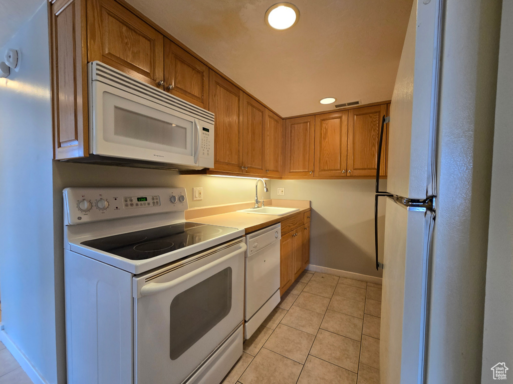Kitchen featuring light tile patterned floors, brown cabinets, white appliances, and a sink