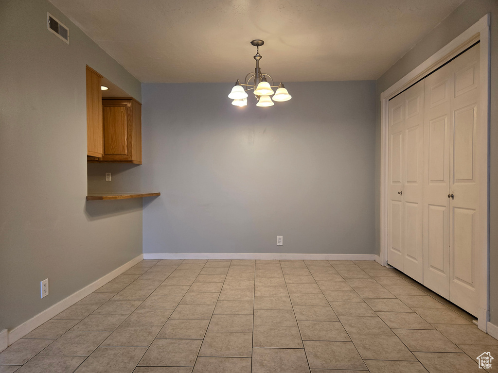 Unfurnished dining area featuring an inviting chandelier, light tile patterned floors, baseboards, and visible vents