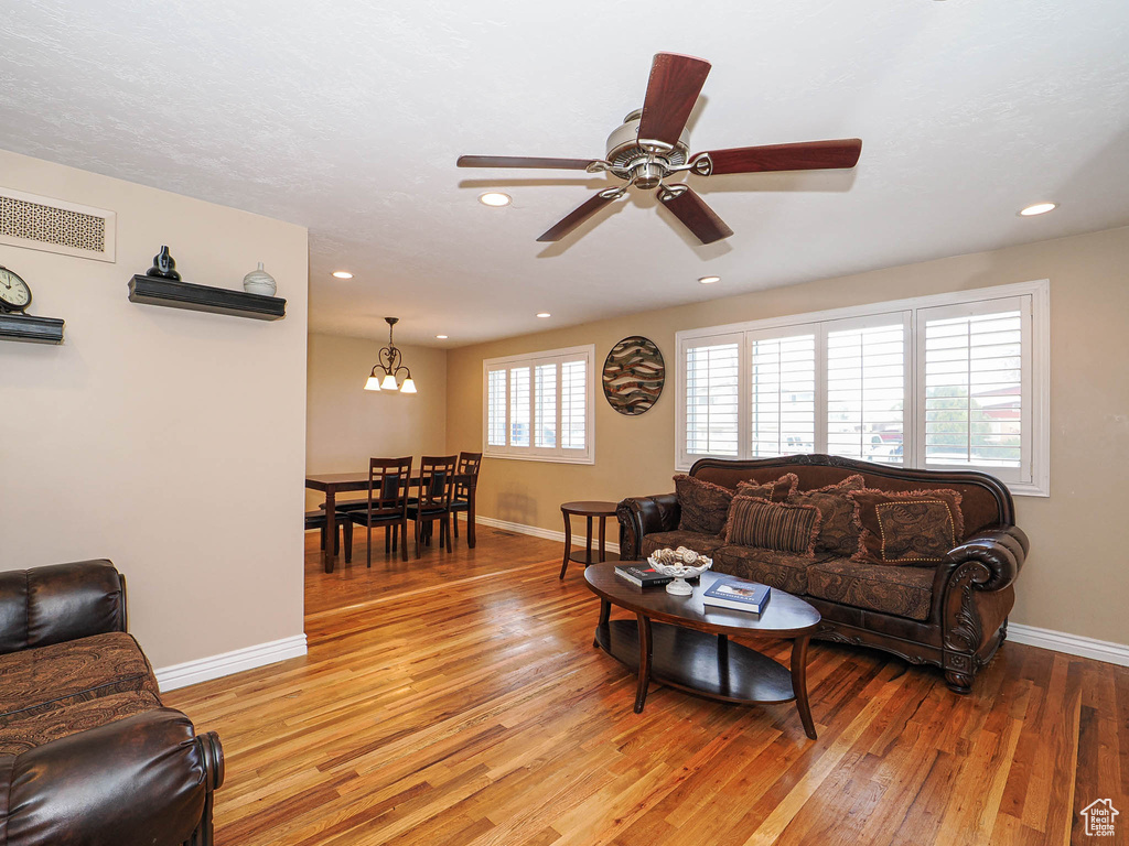 Living area with light wood finished floors, visible vents, ceiling fan with notable chandelier, and baseboards