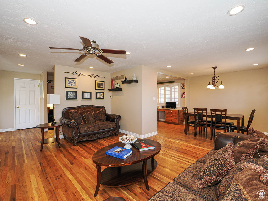 Living room with baseboards, recessed lighting, ceiling fan with notable chandelier, light wood-style floors, and a textured ceiling