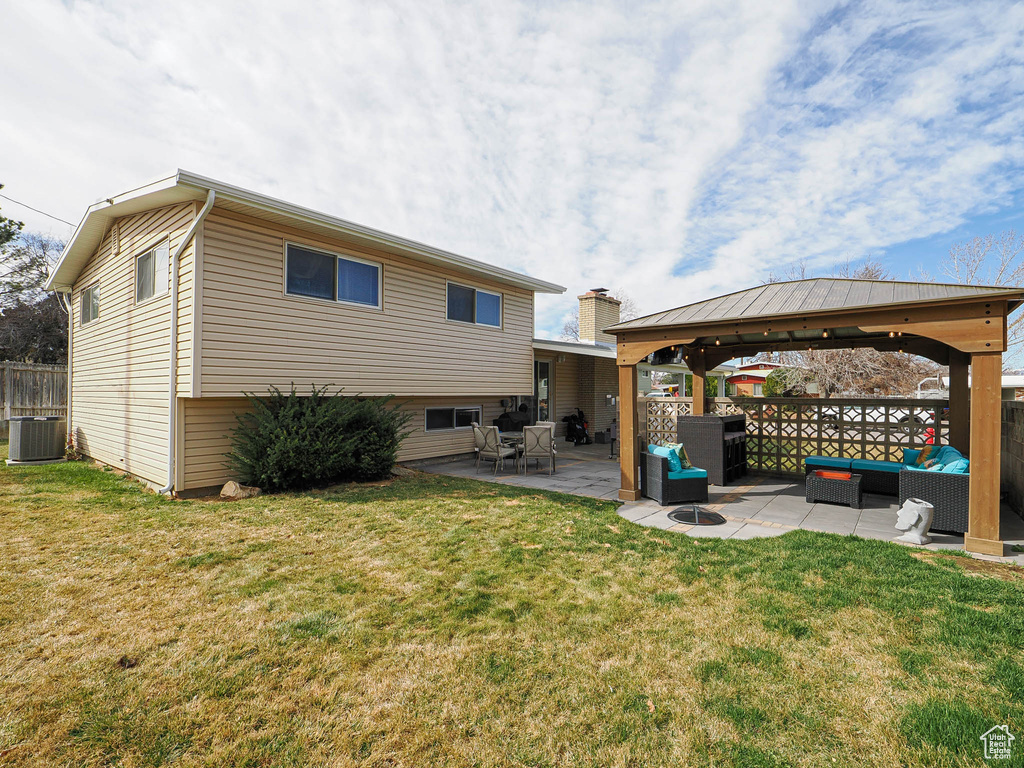 Rear view of house featuring fence, central AC unit, an outdoor living space, a gazebo, and a lawn