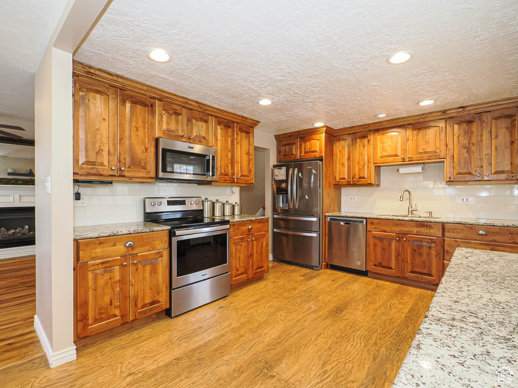 Kitchen featuring light stone counters, decorative backsplash, brown cabinets, appliances with stainless steel finishes, and light wood-style floors
