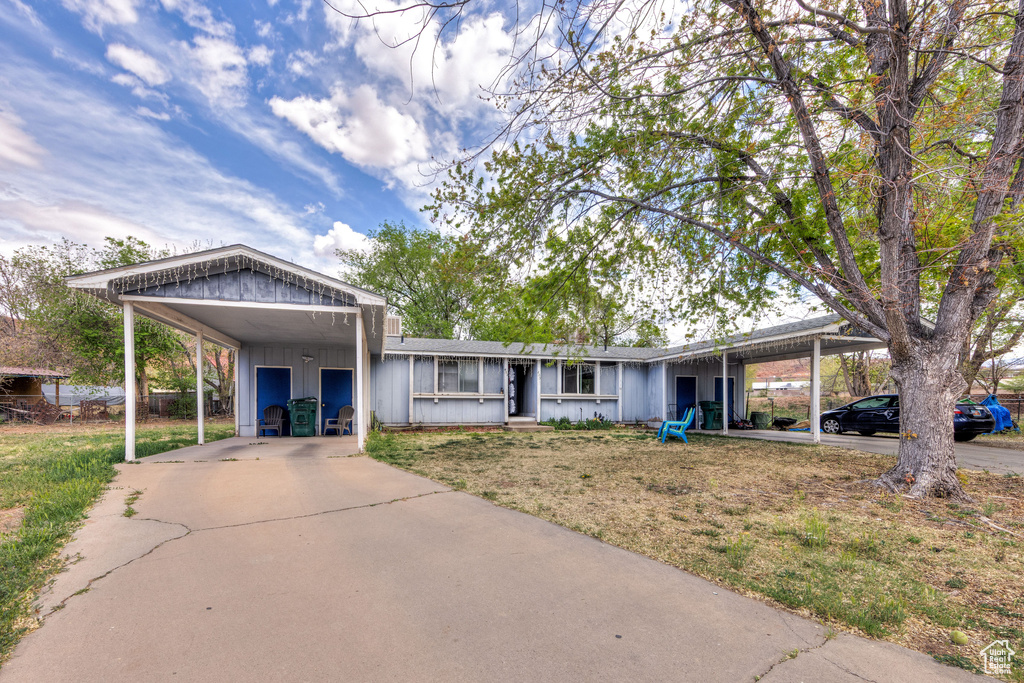 View of front of property featuring driveway, board and batten siding, an attached carport, and a front lawn